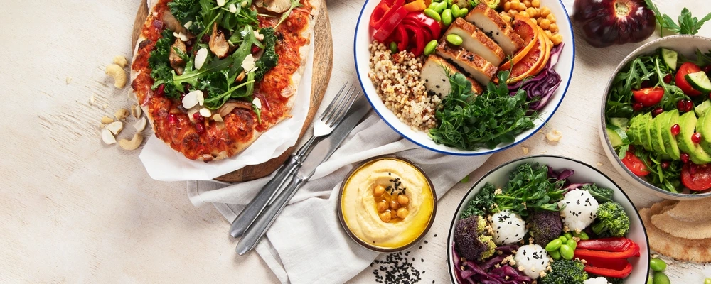 Verschiedene bunte vegetarische Gerichte wie Bowls, Pizza und Salate, die eine ausgewogene Ernährung nach der Ernährungspyramide vegetarisch veranschaulichen.