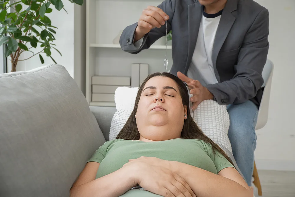 Frau liegt entspannt auf einem Sofa, während ein Therapeut eine Hypnosesitzung zur Unterstützung beim Hypnose abnehmen durchführt.