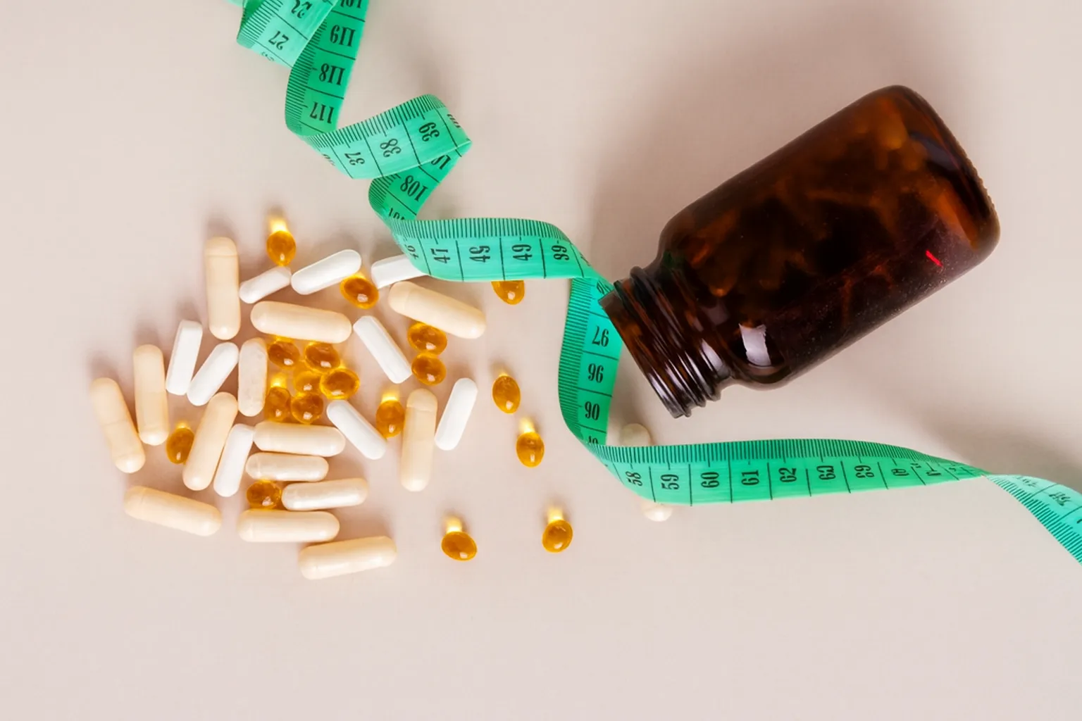 Auf einem Tisch liegen verstreute Abnehmtabletten neben einer geöffneten braunen Pillendose und einem Maßband als Symbol für Gewichtsabnahme.