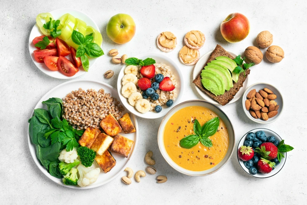 Verschiedene kalorienarme Lebensmittel wie Gemüse, Obst, Nüsse, Vollkornbrot und Suppe sind appetitlich auf Tellern angerichtet.
