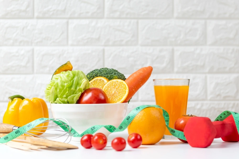 Frisches Gemüse, Obst und ein Glas Saft mit Maßband und Hantel symbolisieren abnehmen durch Ernährungsumstellung.