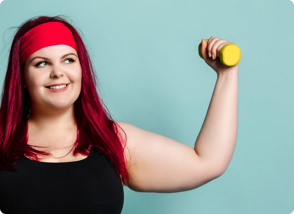 Lächelnde Frau mit rotem Stirnband hebt eine gelbe Kurzhantel vor türkisfarbenem Hintergrund – gelenkschonendes Training.