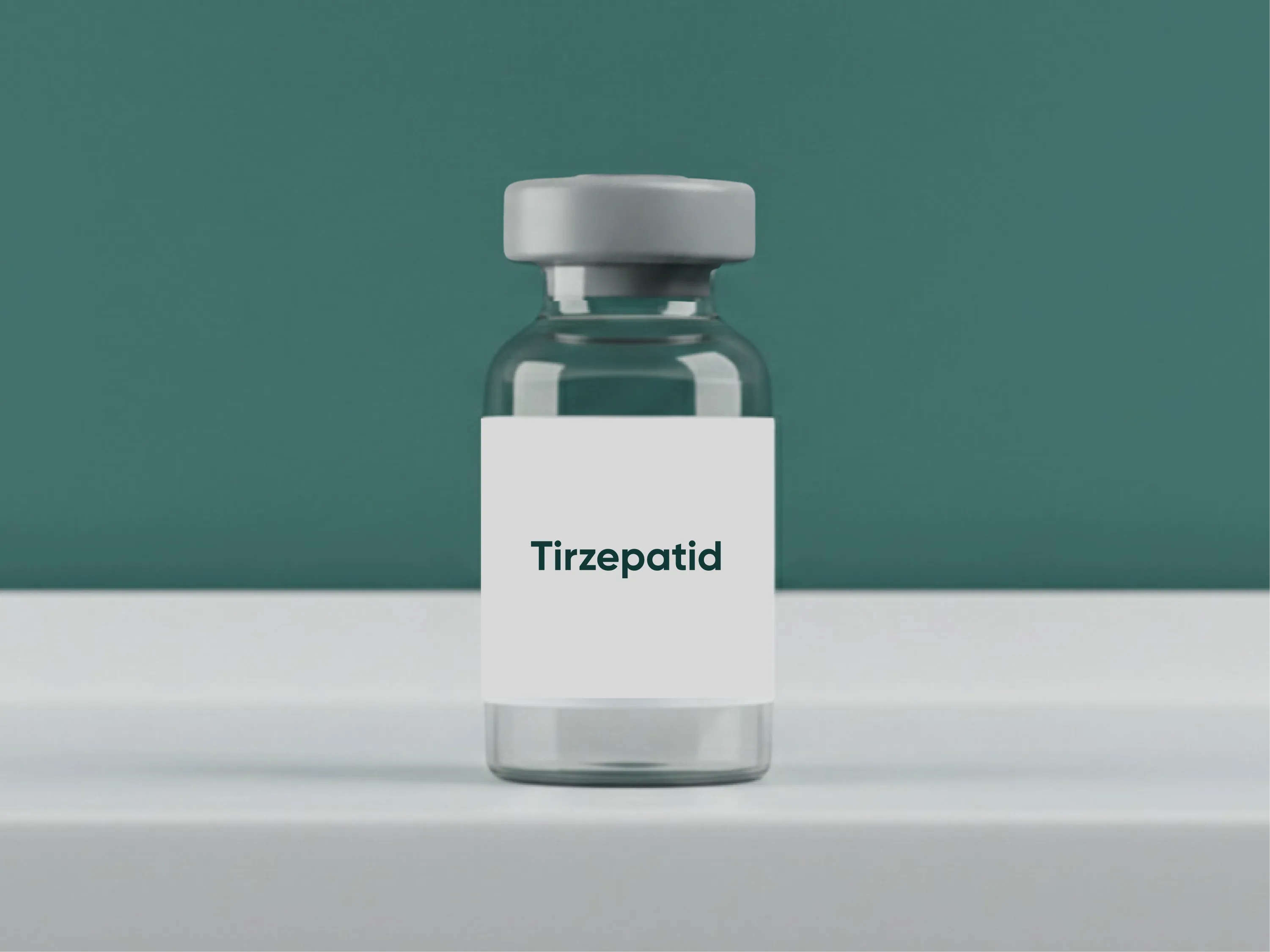 Glasfläschchen mit der Aufschrift Tirzepatid auf weißem Tisch vor grünem Hintergrund als Darstellung eines Wirkstoffes zur Gewichtsreduktion.