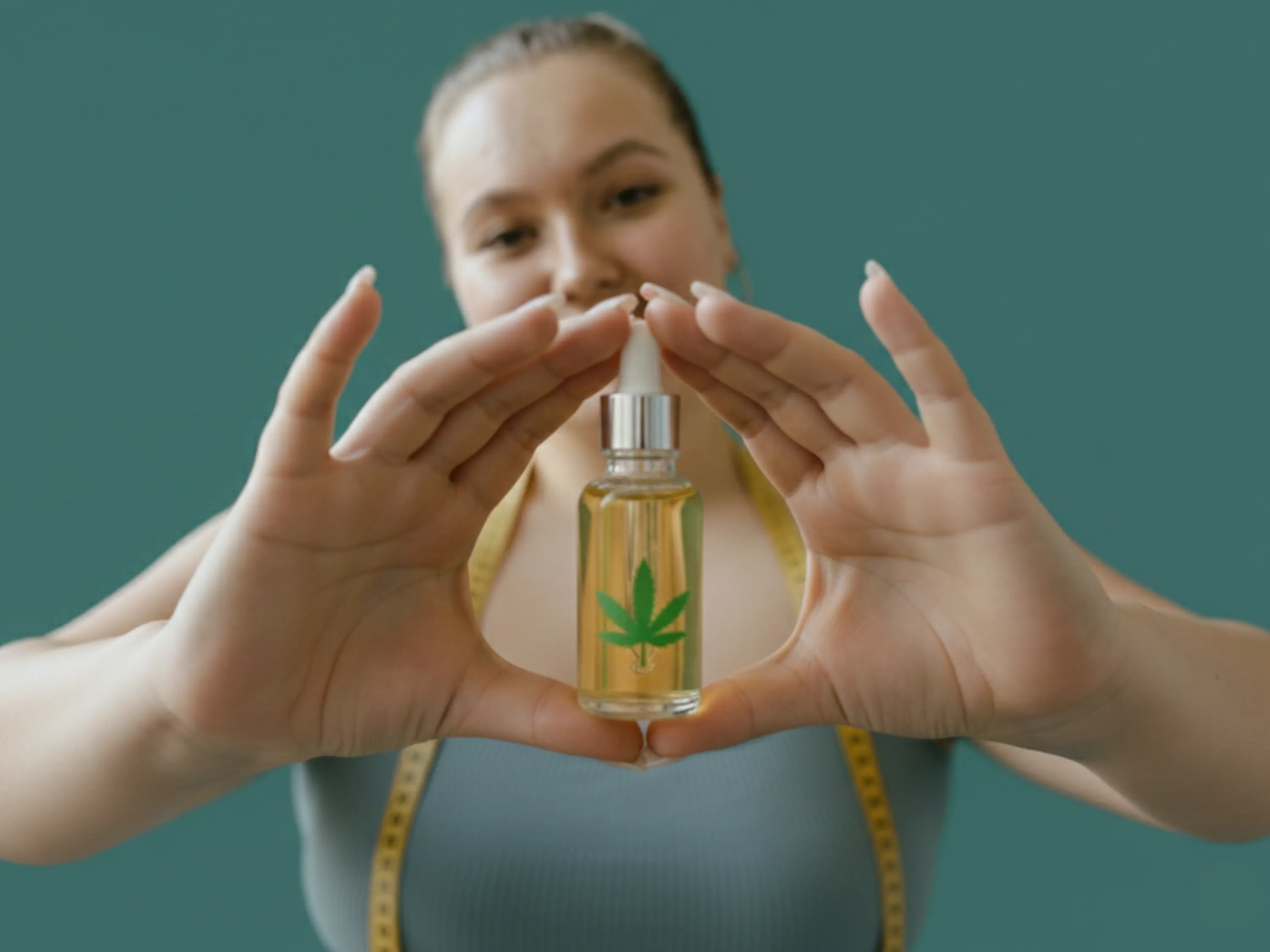 Frau hält eine Pipettenflasche mit Hanfblatt-Symbol in den Händen – Symbolbild für CBD Öl zum Abnehmen und mögliche Wirkung auf das Gewicht.