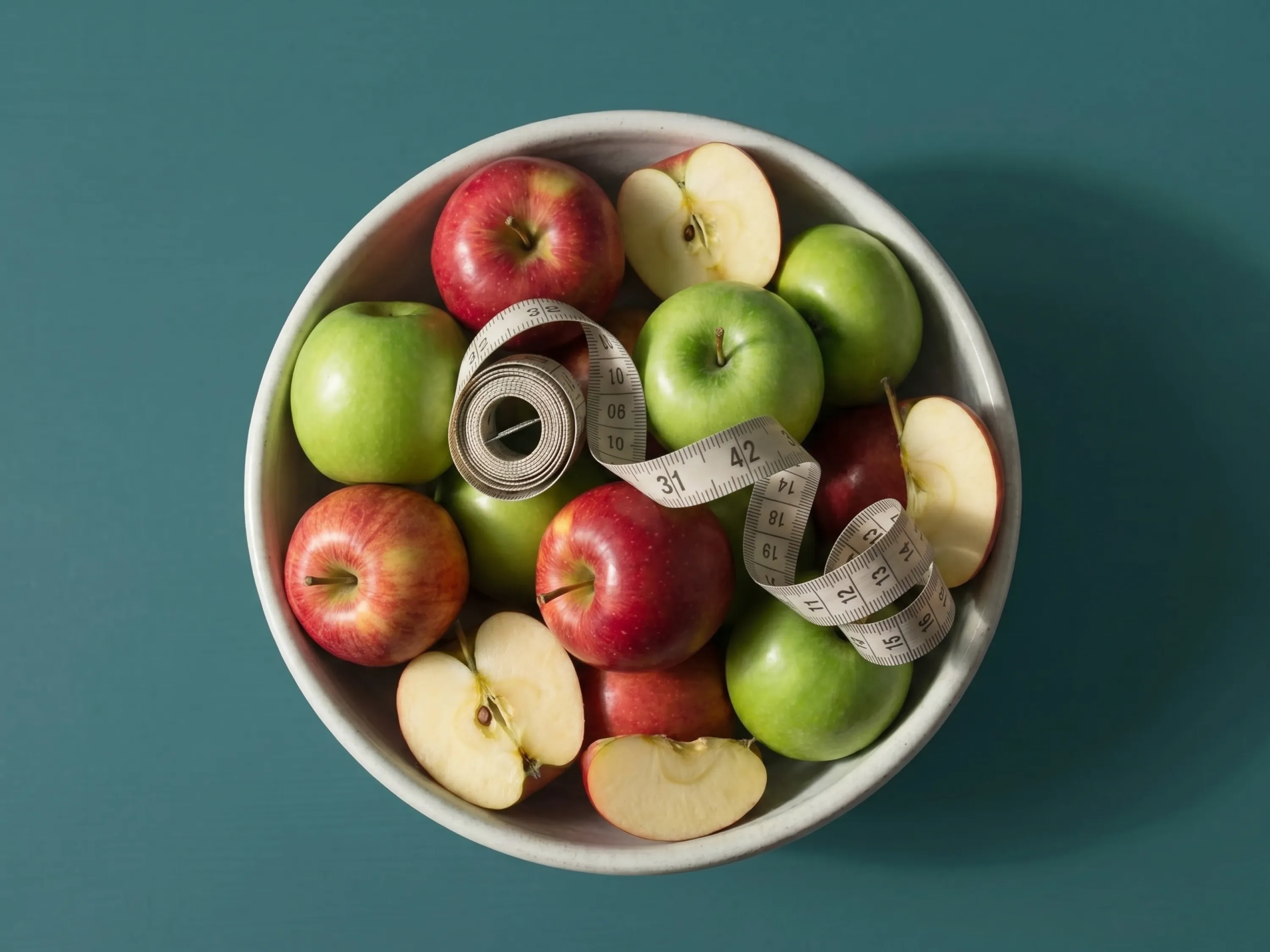 Eine Schale voller Äpfel und ein Maßband veranschaulichen das Prinzip der Apfel-Diät.