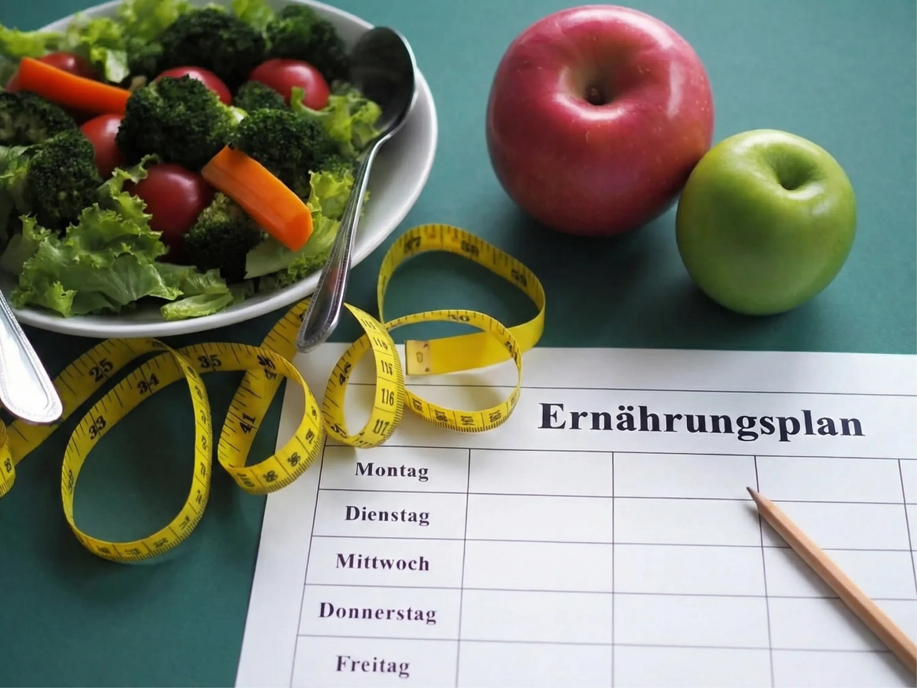Auf grünem Hintergrund liegen frisches Gemüse, Äpfel, ein Maßband und ein Blatt mit Wochentagen – alles als Symbol für einen Ernährungsplan zum Abnehmen.