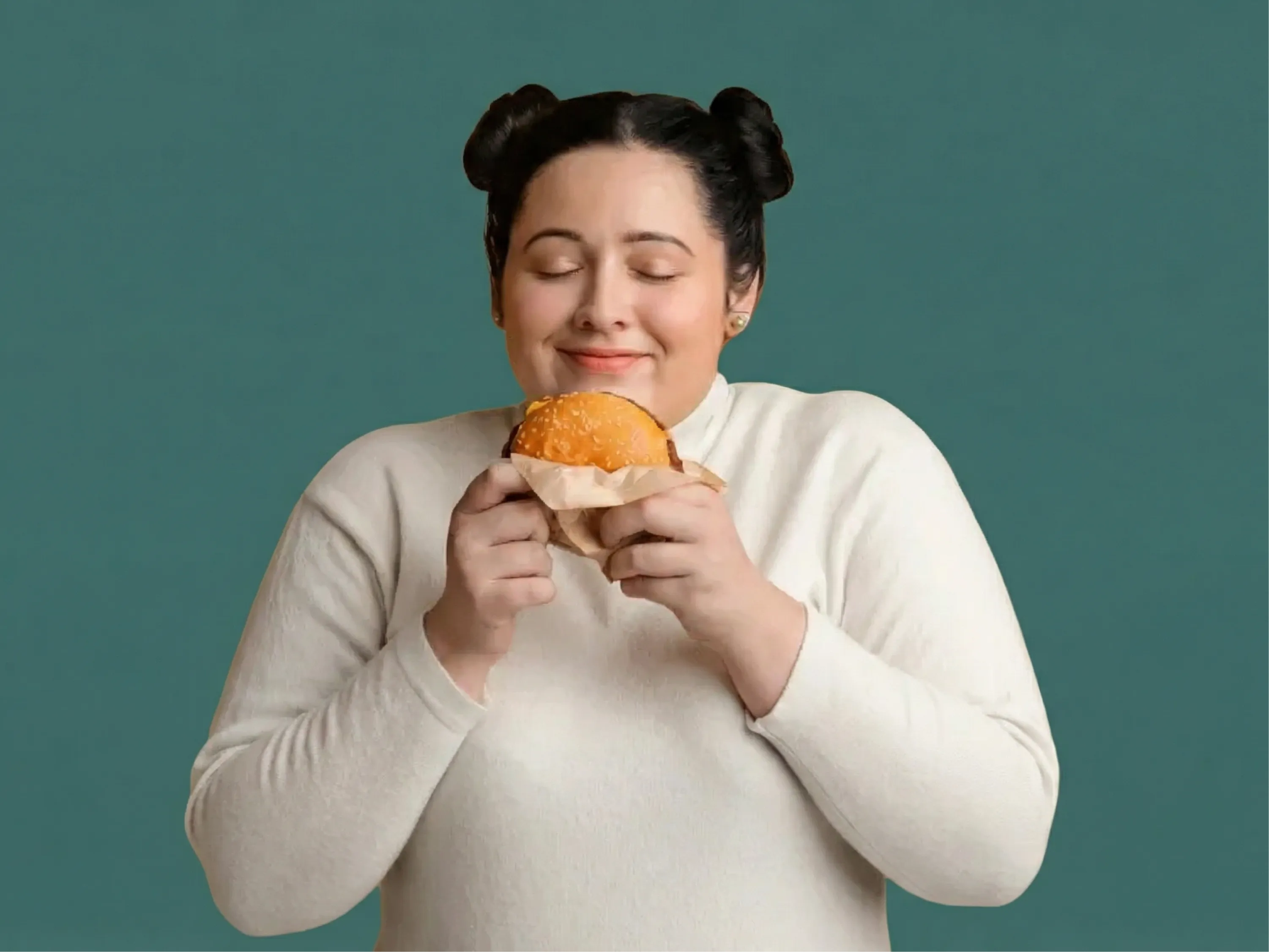 Junge Frau hält genüsslich einen Burger in den Händen und schließt die Augen vor Freude – ein typisches Bild für starken Heißhunger auf ungesunde Lebensmittel.
