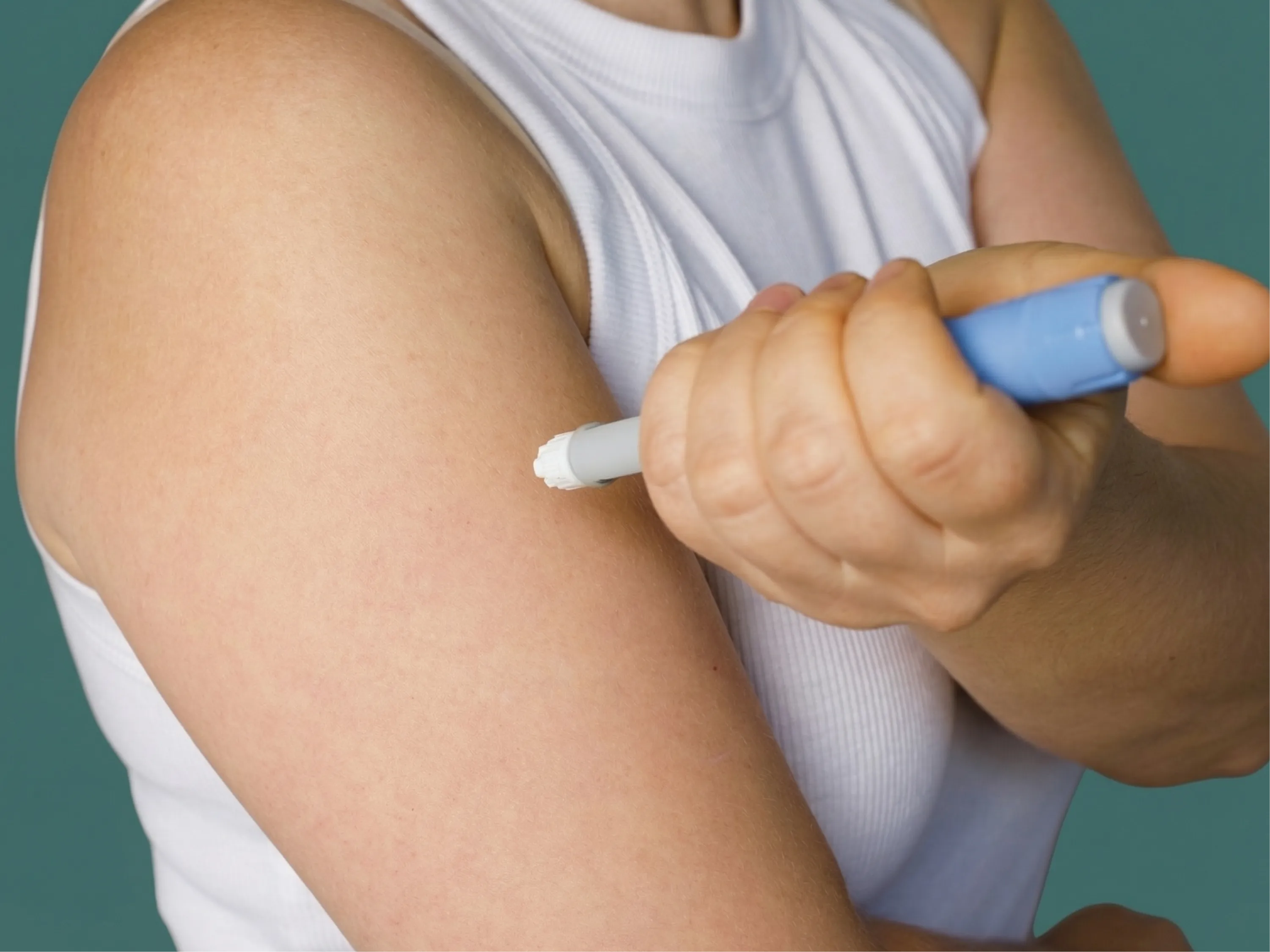 Person setzt einen Injektionspen am Oberarm an, um Insulin zum abnehmen zu verwenden.
