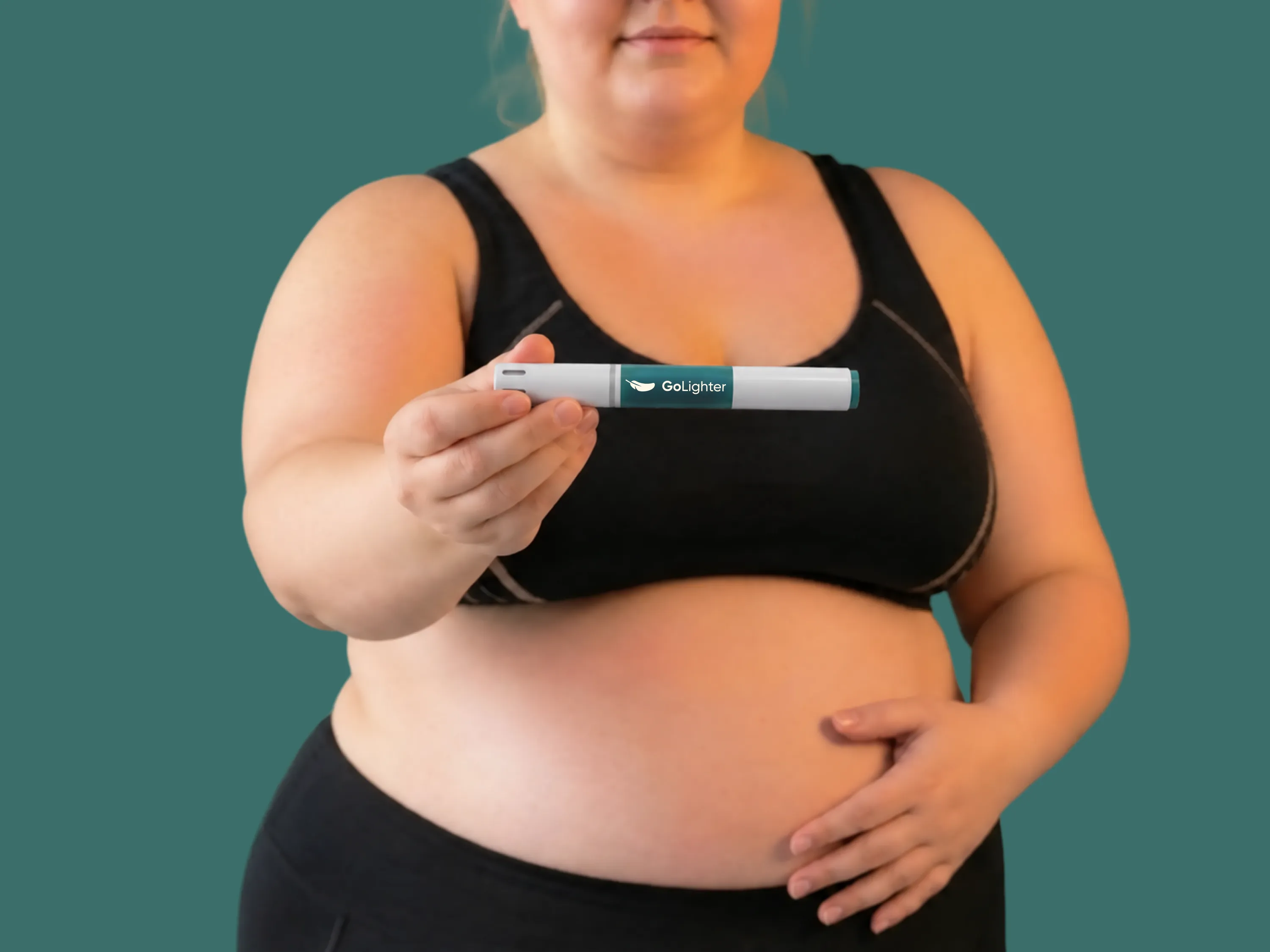 Eine Frau in schwarzer Sportkleidung hält einen Mounjaro 2,5 mg Pen und legt eine Hand auf ihren Bauch.