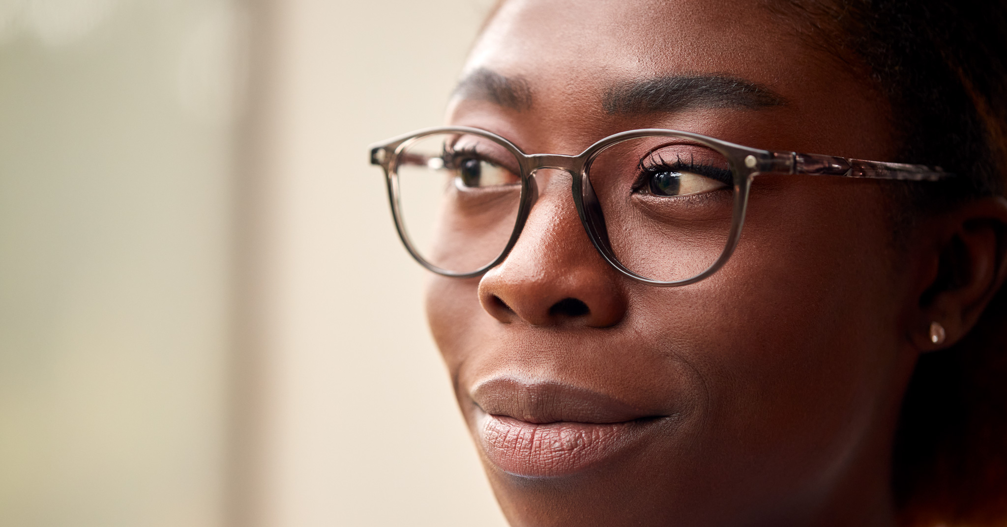 Woman wearing glasses looking thoughtfully to the side in soft light