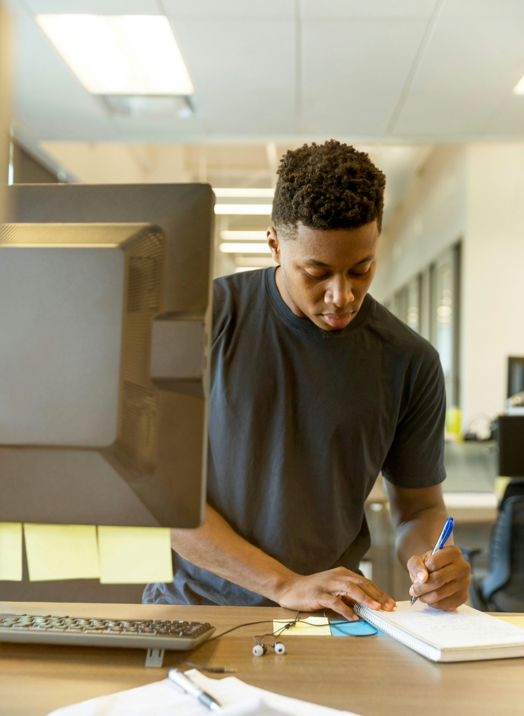 Young person studying and taking notes at computer workspace