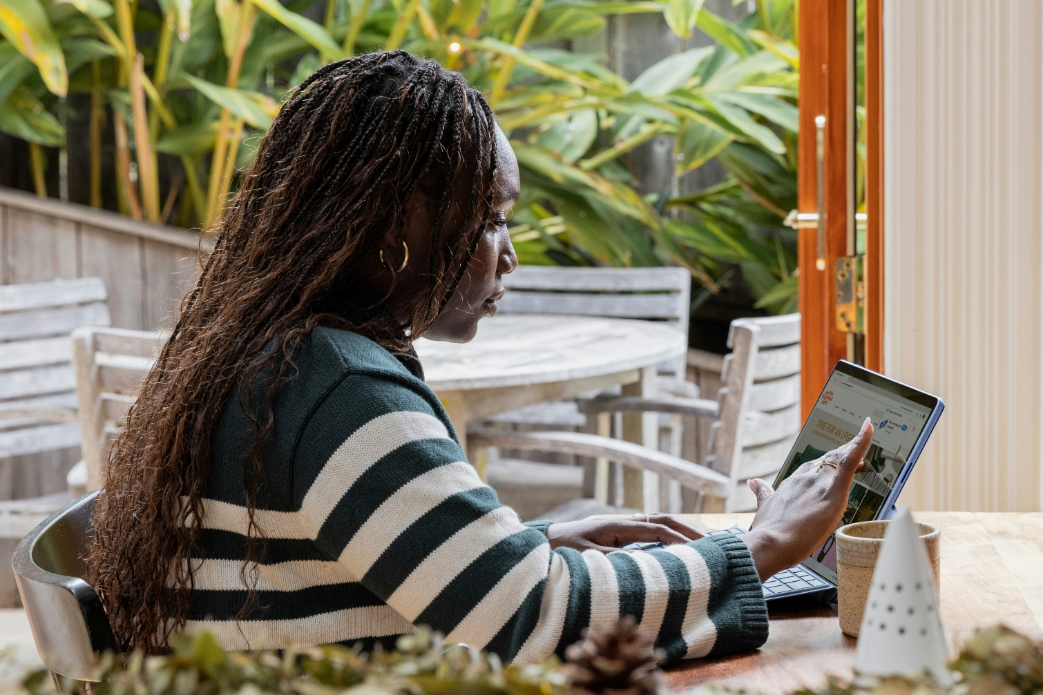 Person working on tablet at outdoor table surrounded by plants