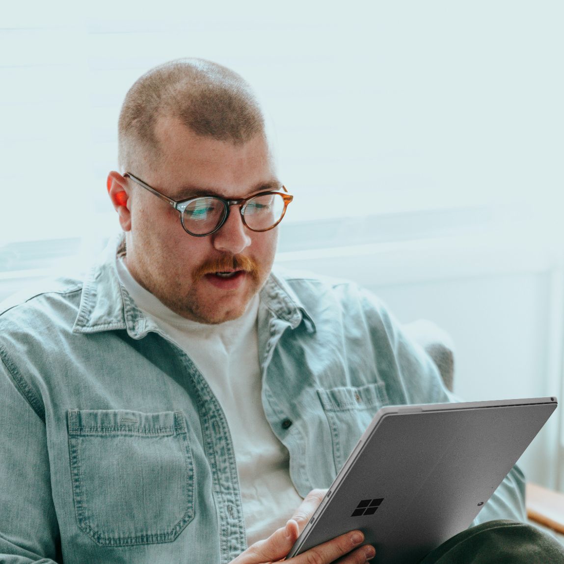 Person in denim shirt using a Surface tablet near a window