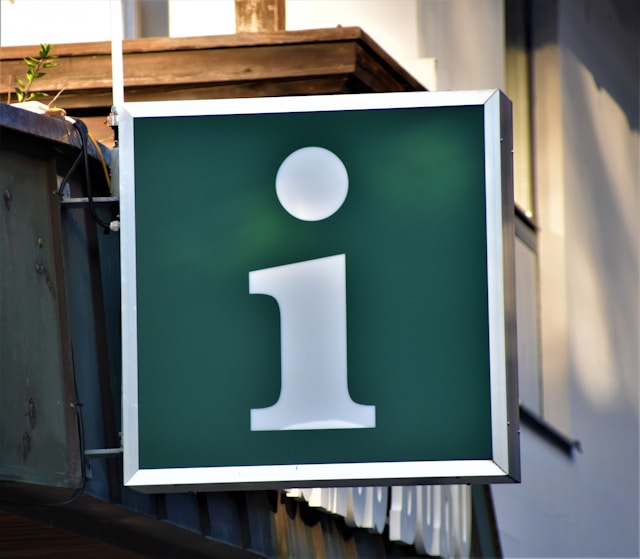 Green information sign with white 'i' symbol hanging outdoors
