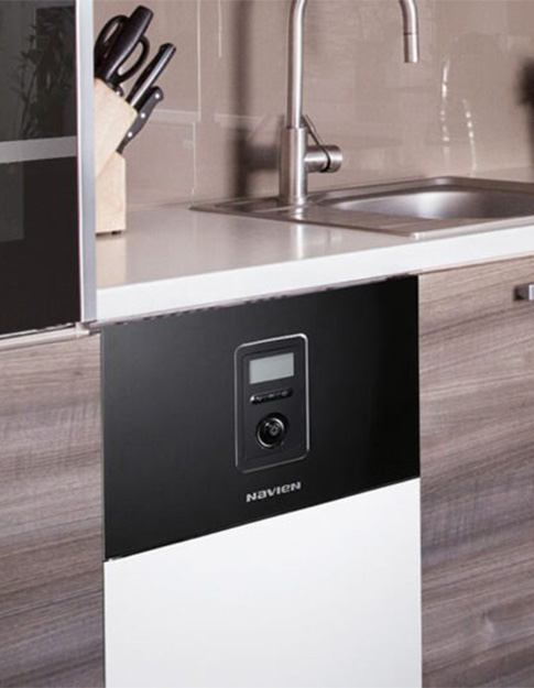 Navien oil boiler installed under a kitchen countertop next to a stainless steel sink and a knife block.