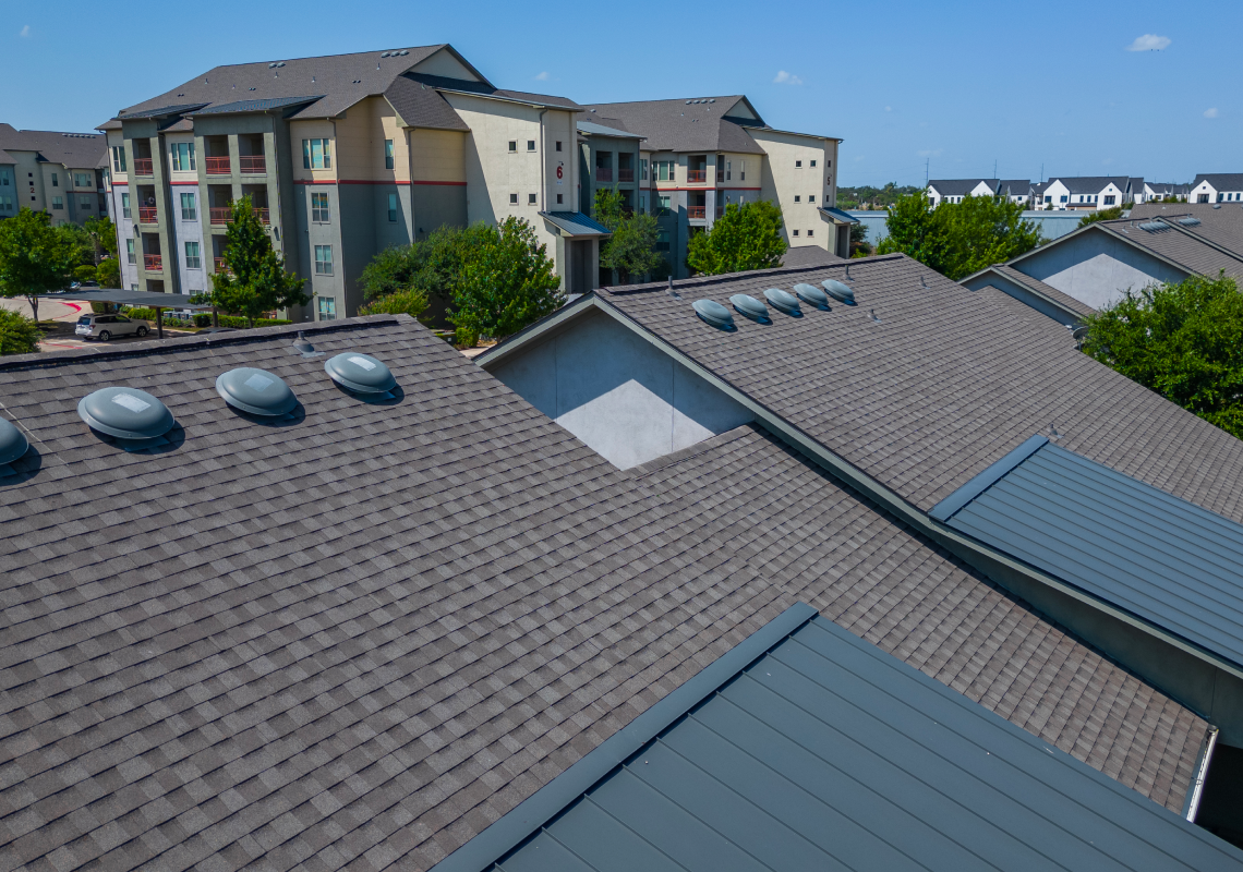 residential rooftops with asphalt shingles and roof ventilation units in suburban area