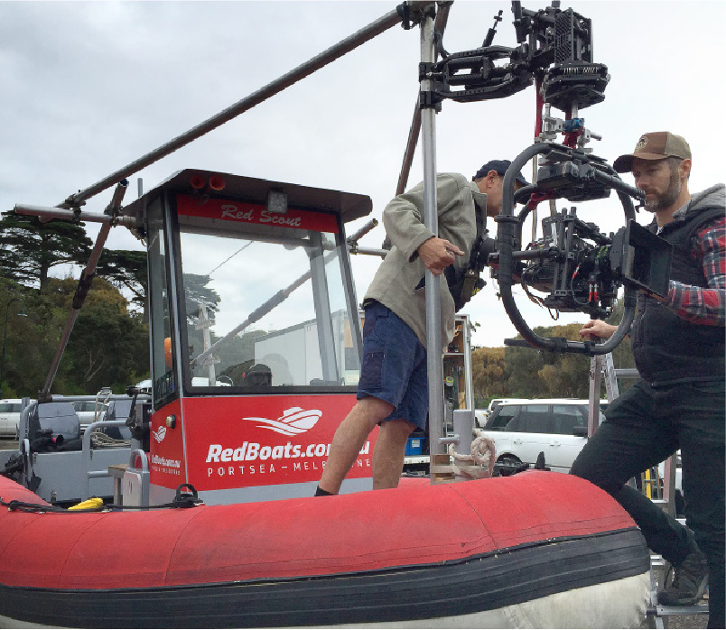 Two men adjusting a professional camera rig on a red inflatable boat with Red Boats Portsea Melbourne branding.