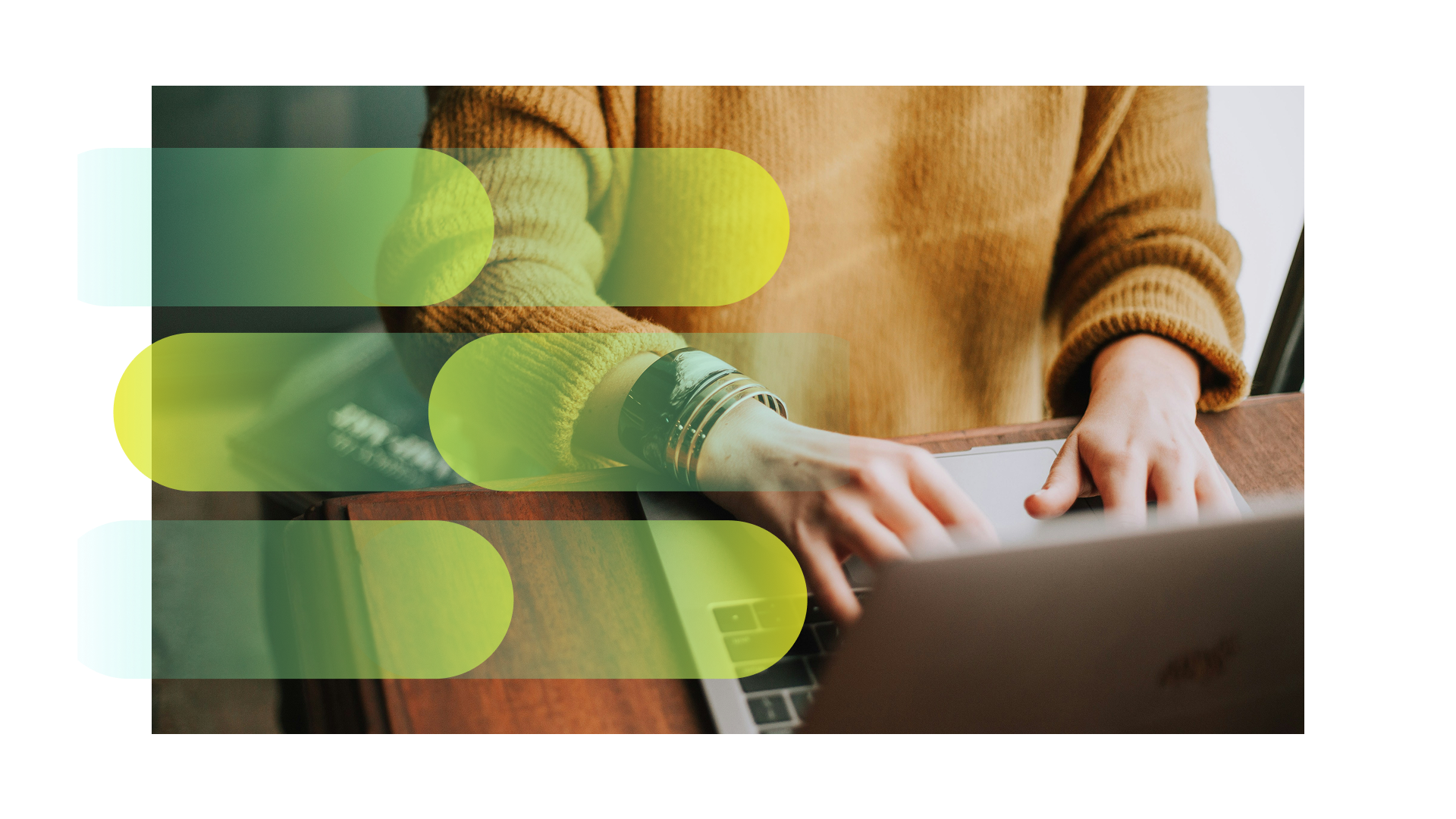 Person wearing a brown sweater typing on a laptop keyboard at a wooden desk.