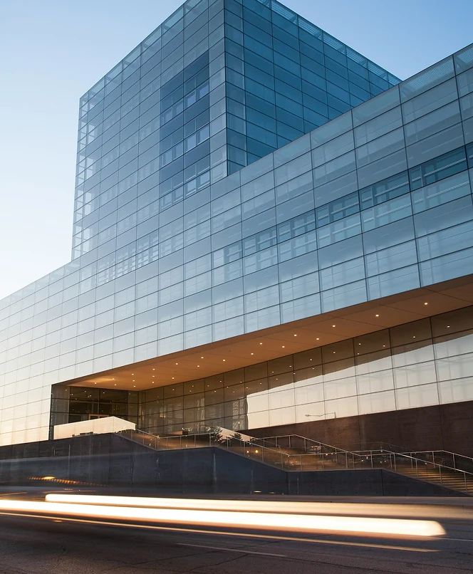 Modern glass office building with a sloped ramp and light trails on the road in front.