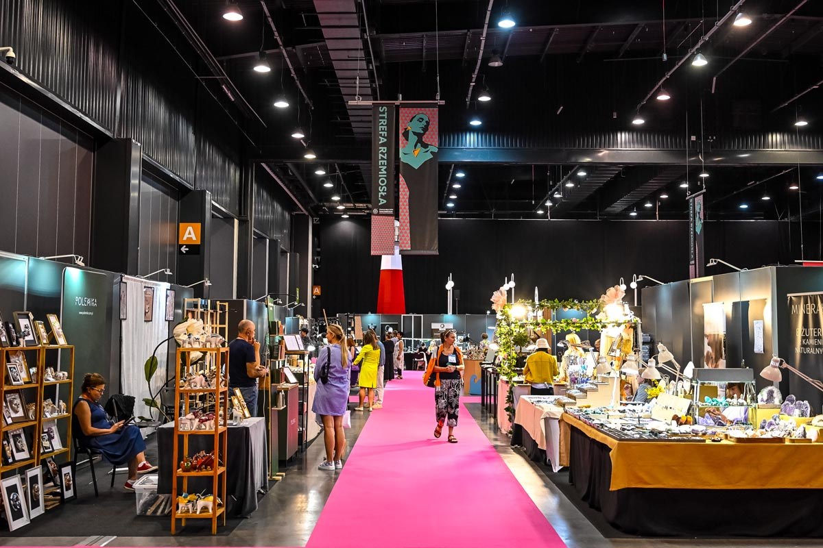 Alejka Strefy Rzemiosła w hali Amber Expo, po obu stronach stoiska z ceramiką, grafikami i biżuterią