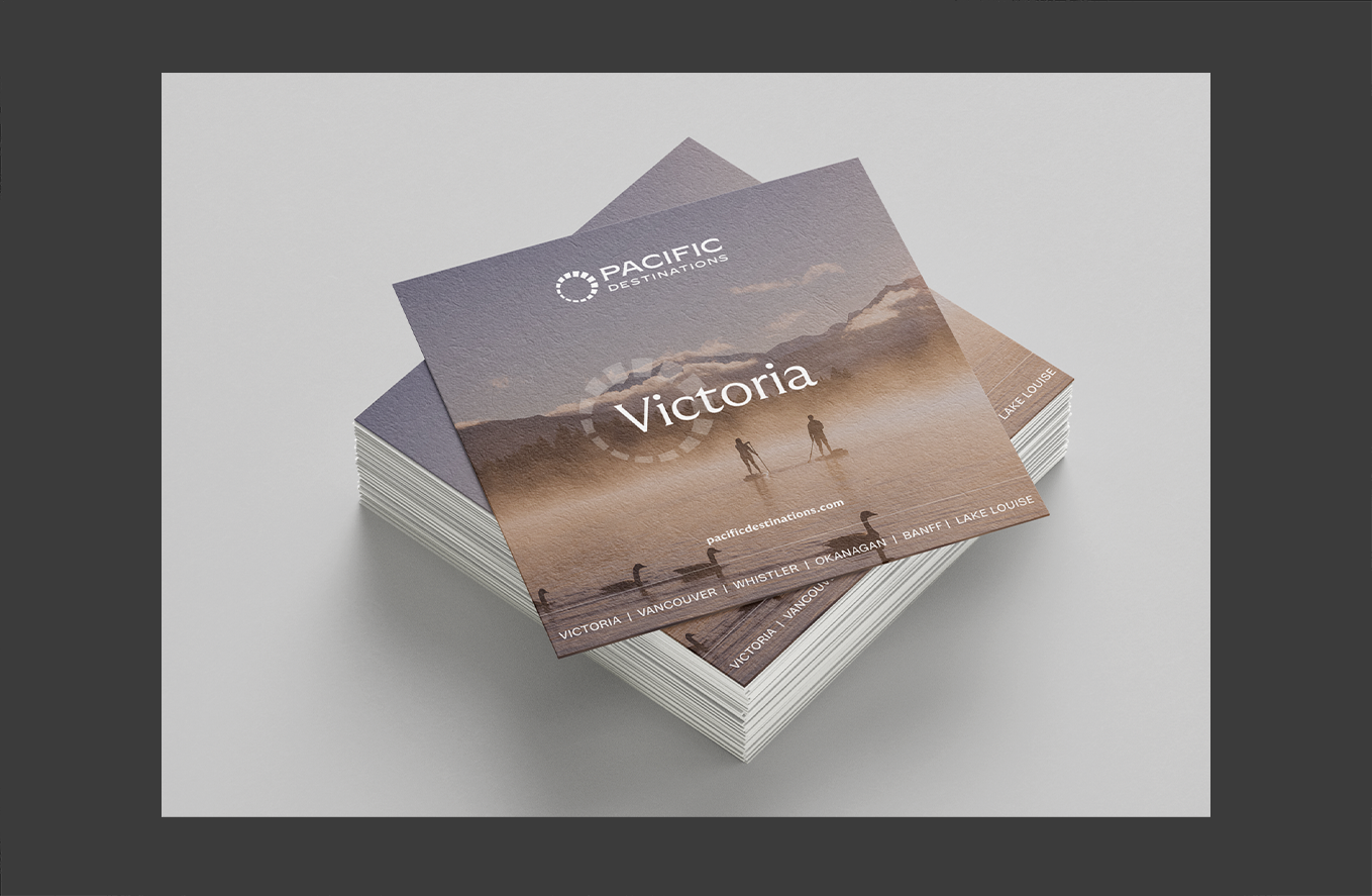 Stack of brochures for Pacific Destinations featuring a misty lake scene with two paddleboarders at sunrise.