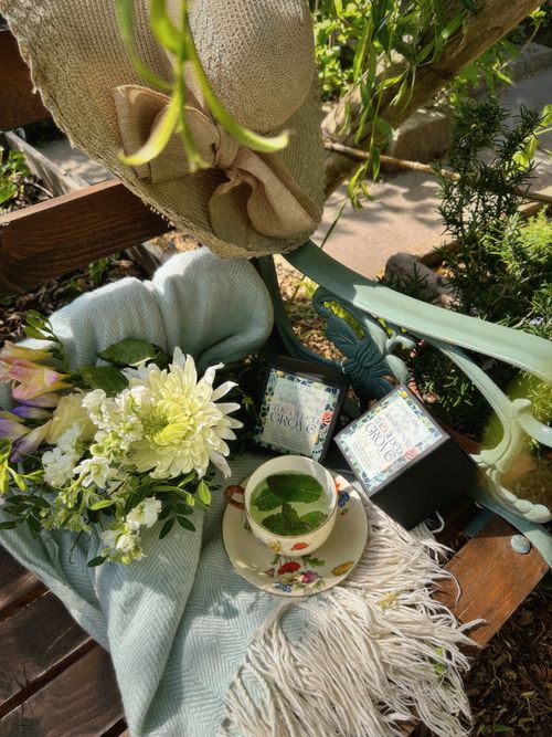 Hand-poured coconut wax Gilded Grove candles by Golly Gosh Candles with floral packaging, styled in a garden setting with flowers, tea, and summer decor.