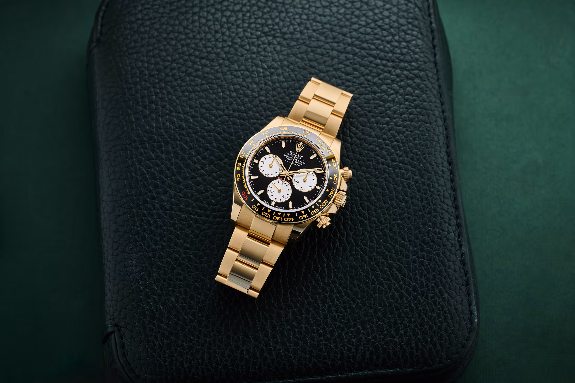 A dramatic eagle-eye shot of the 18k gold Rolex Daytona Le Mans (Ref. 126528LN), highlighting the red "100" on the ceramic bezel against a dark background.