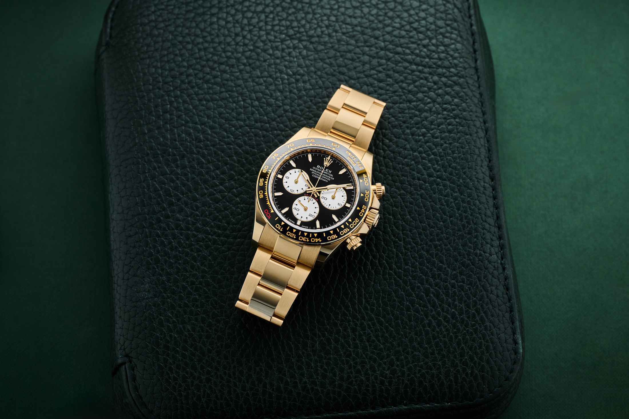 A dramatic eagle-eye shot of the 18k gold Rolex Daytona Le Mans (Ref. 126528LN), highlighting the red "100" on the ceramic bezel against a dark background.