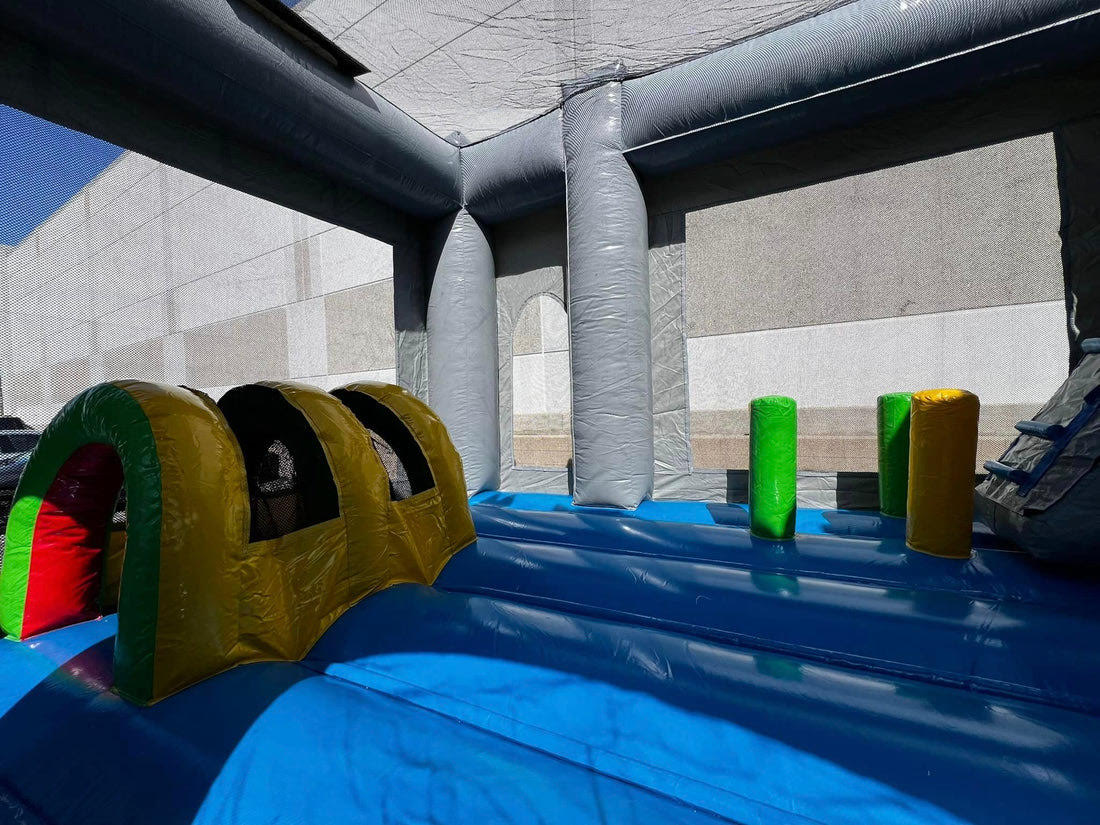 Interior view of the 6-in-1 Dragon Combo inflatable featuring a colorful crawl tunnel and upright obstacle pillars on a blue bouncy floor, set up next to a large building, located near Austin, Texas.