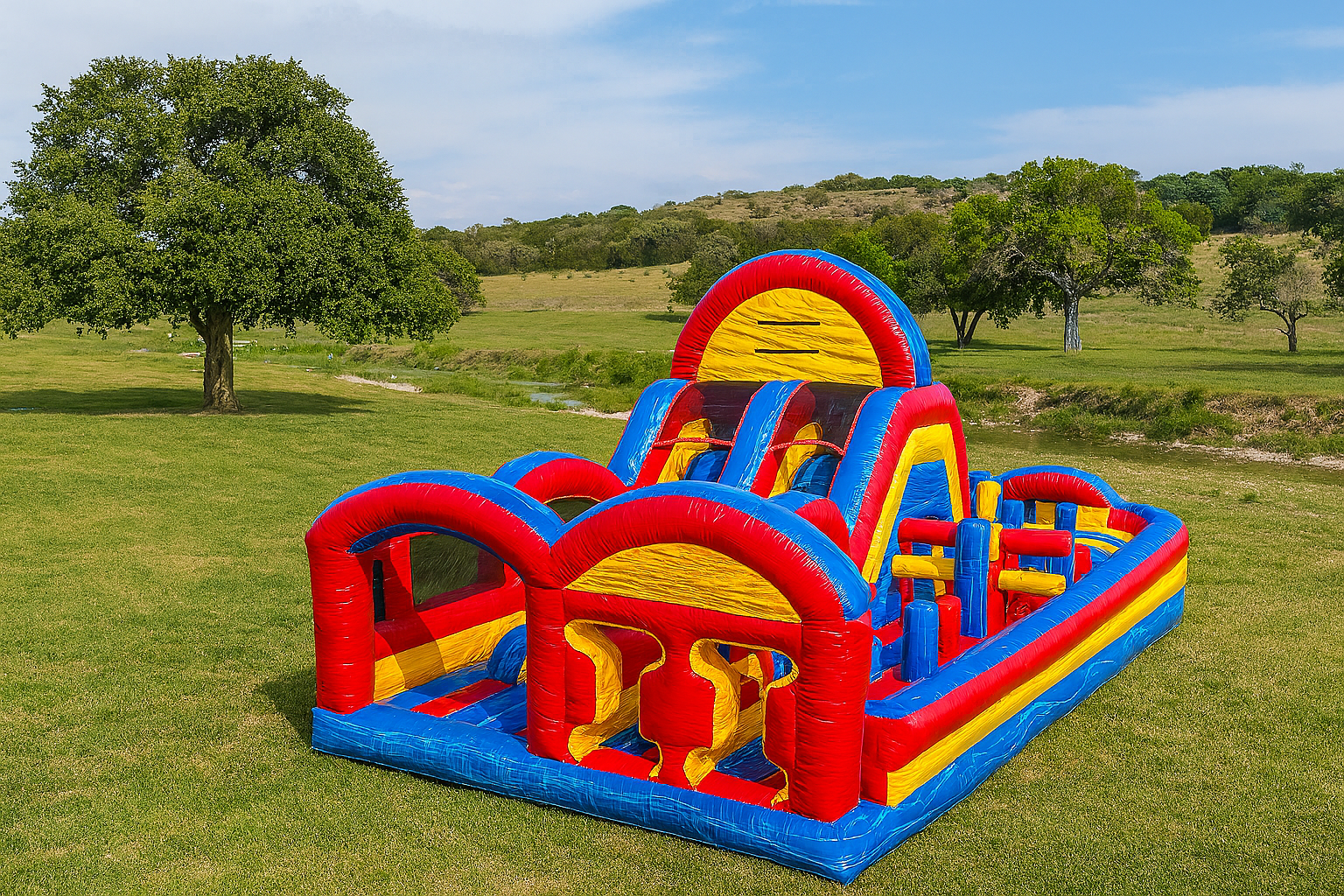 Our Freedom Fun USA Colorful inflatable obstacle course with red, blue, and yellow sections, set up on a grassy field with trees and hills in the background around Waco, Temple, Killeen.