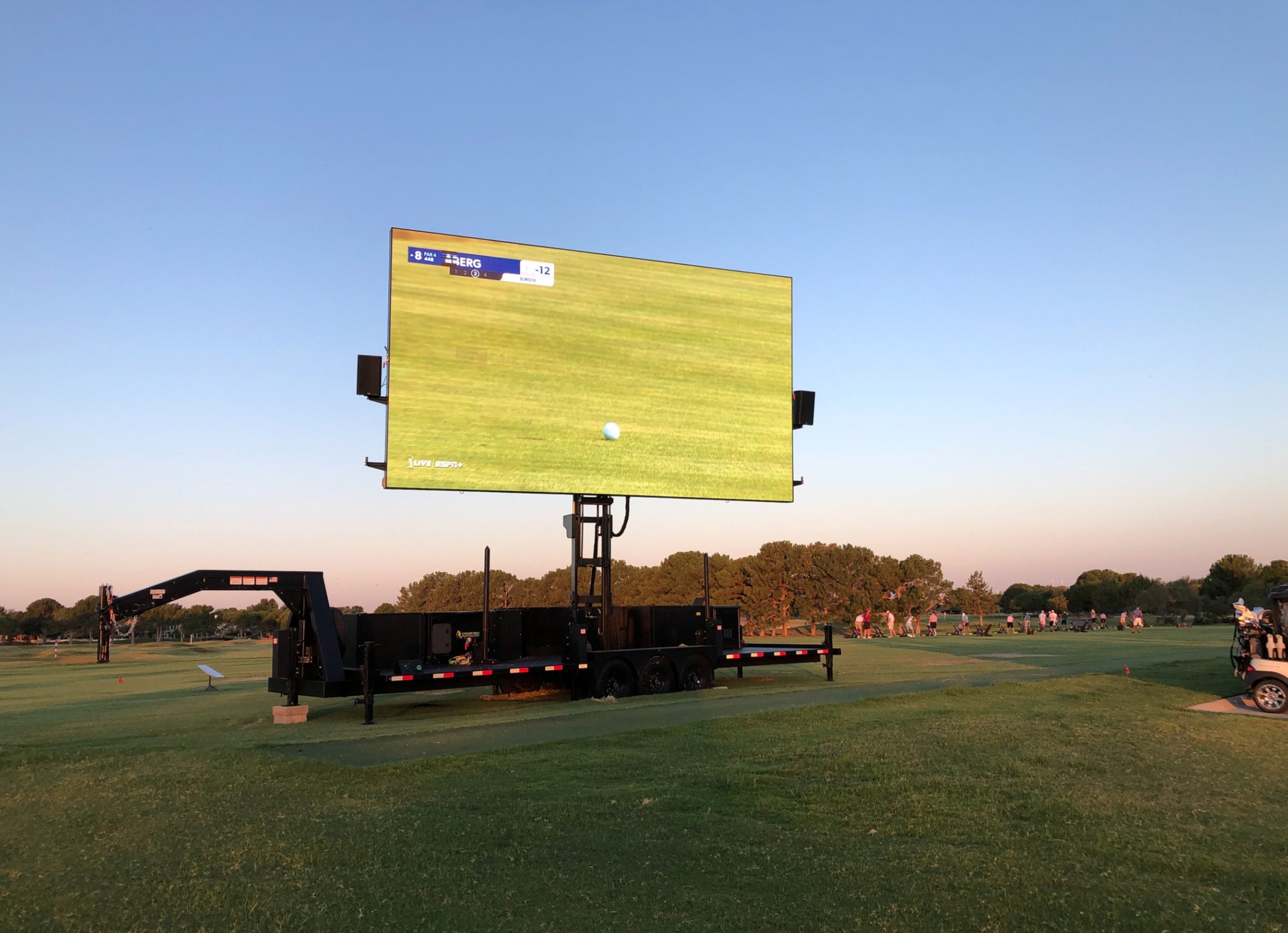 Large mobile LED screen displaying a live golf broadcast on a wide open driving range at sunset, ideal for outdoor watch parties and sporting events.