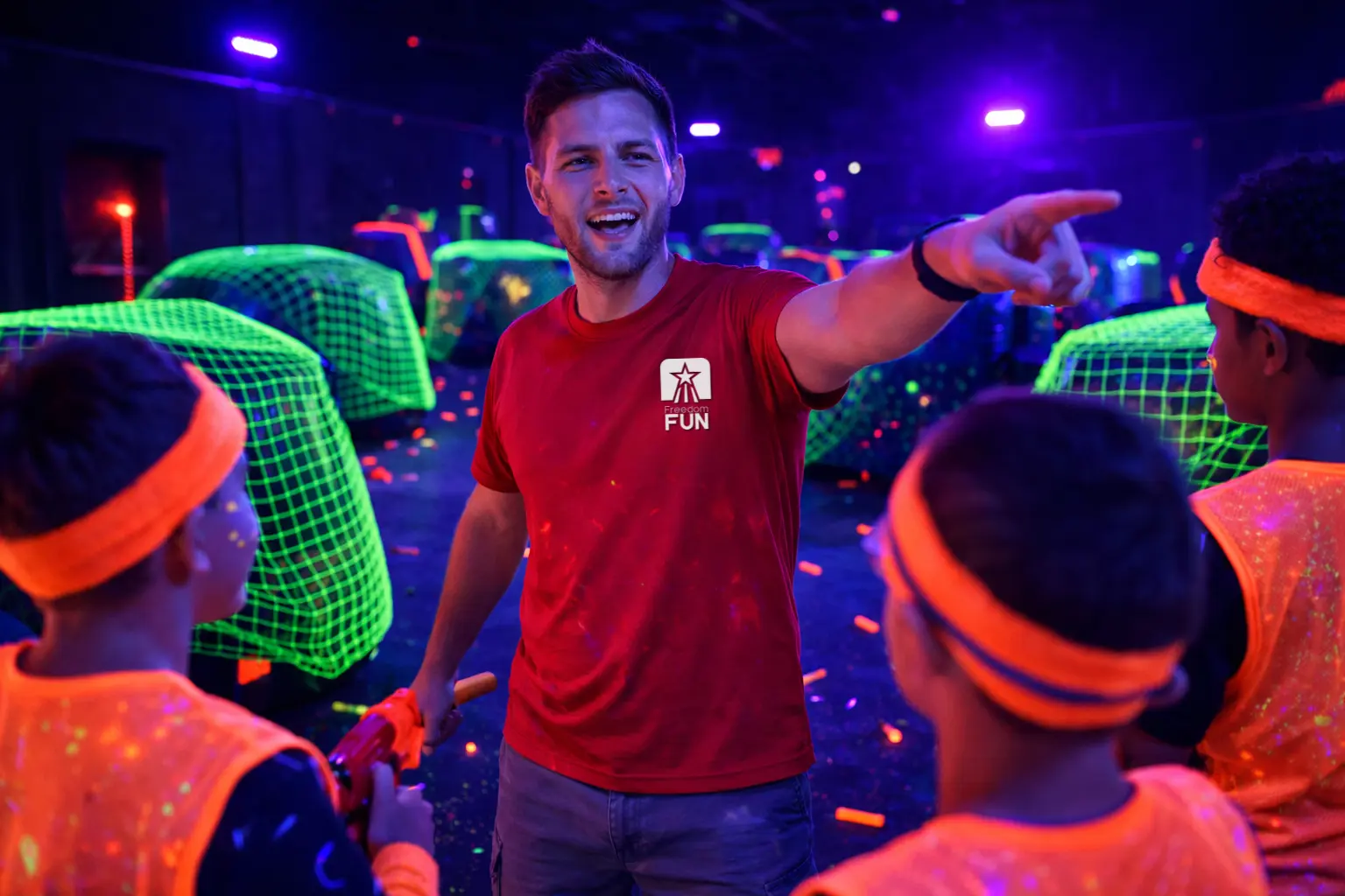 Freedom Fun Event Coach leading a glow Nerf battle with kids in orange vests on a UV-lit blacklight battlefield with neon green netting.