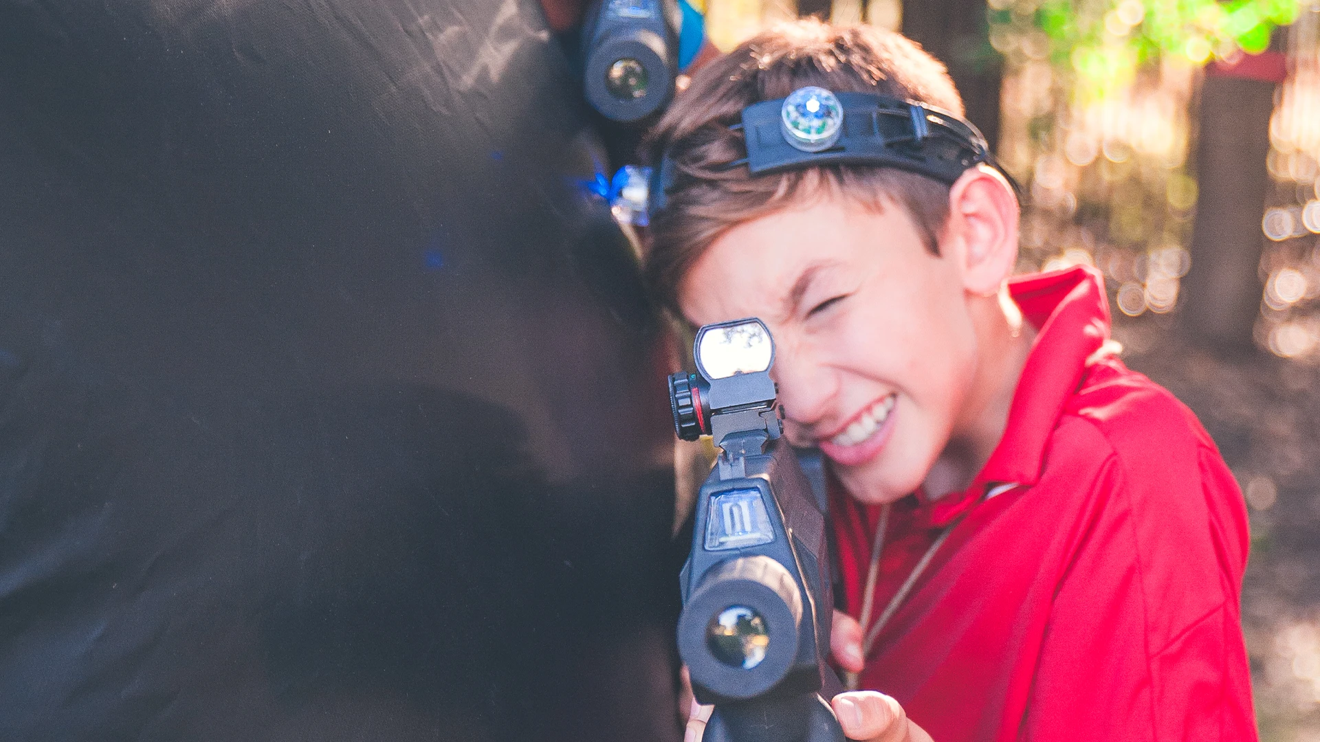 Kid laughing with mobile laser tag rifle and headset during outdoor backyard event