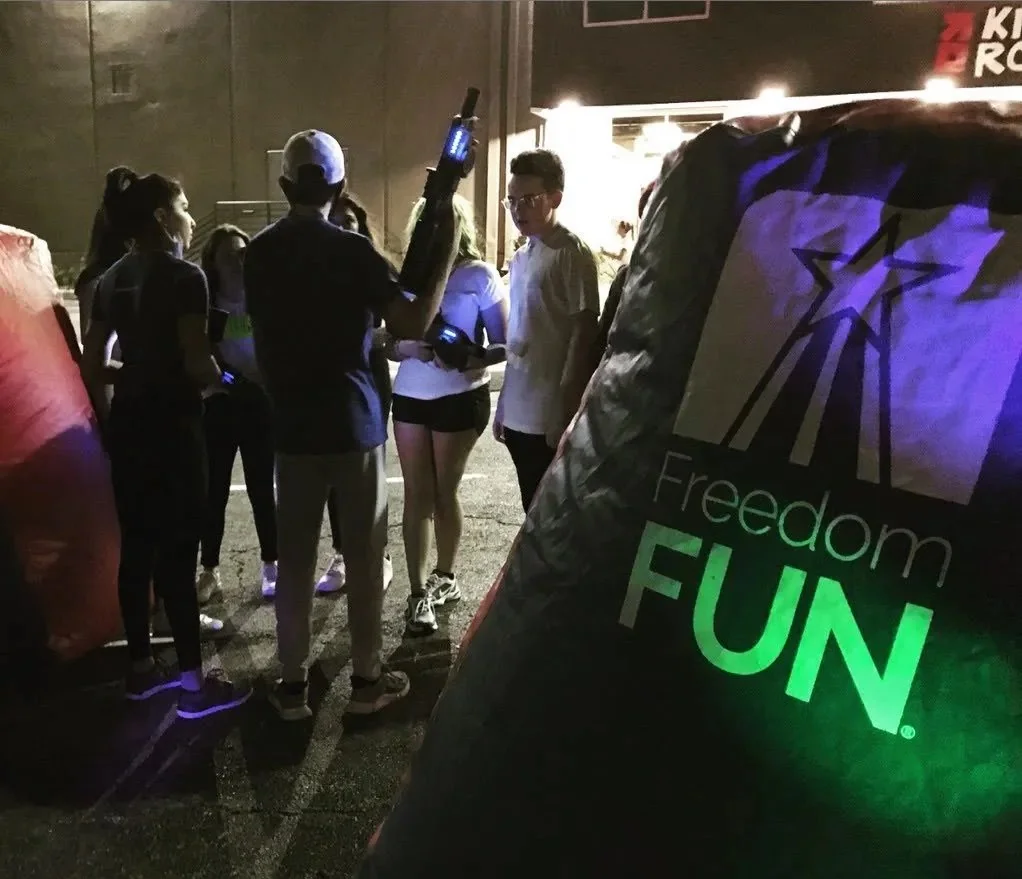 Teen group playing mobile laser tag at night with Freedom Fun branded barricade and LED lighting
