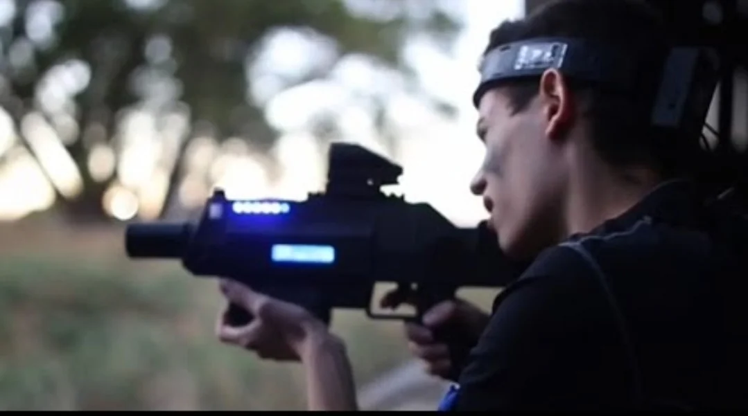 Teen aiming Halo-inspired laser tag battle rifle with LED scope during outdoor sunset event