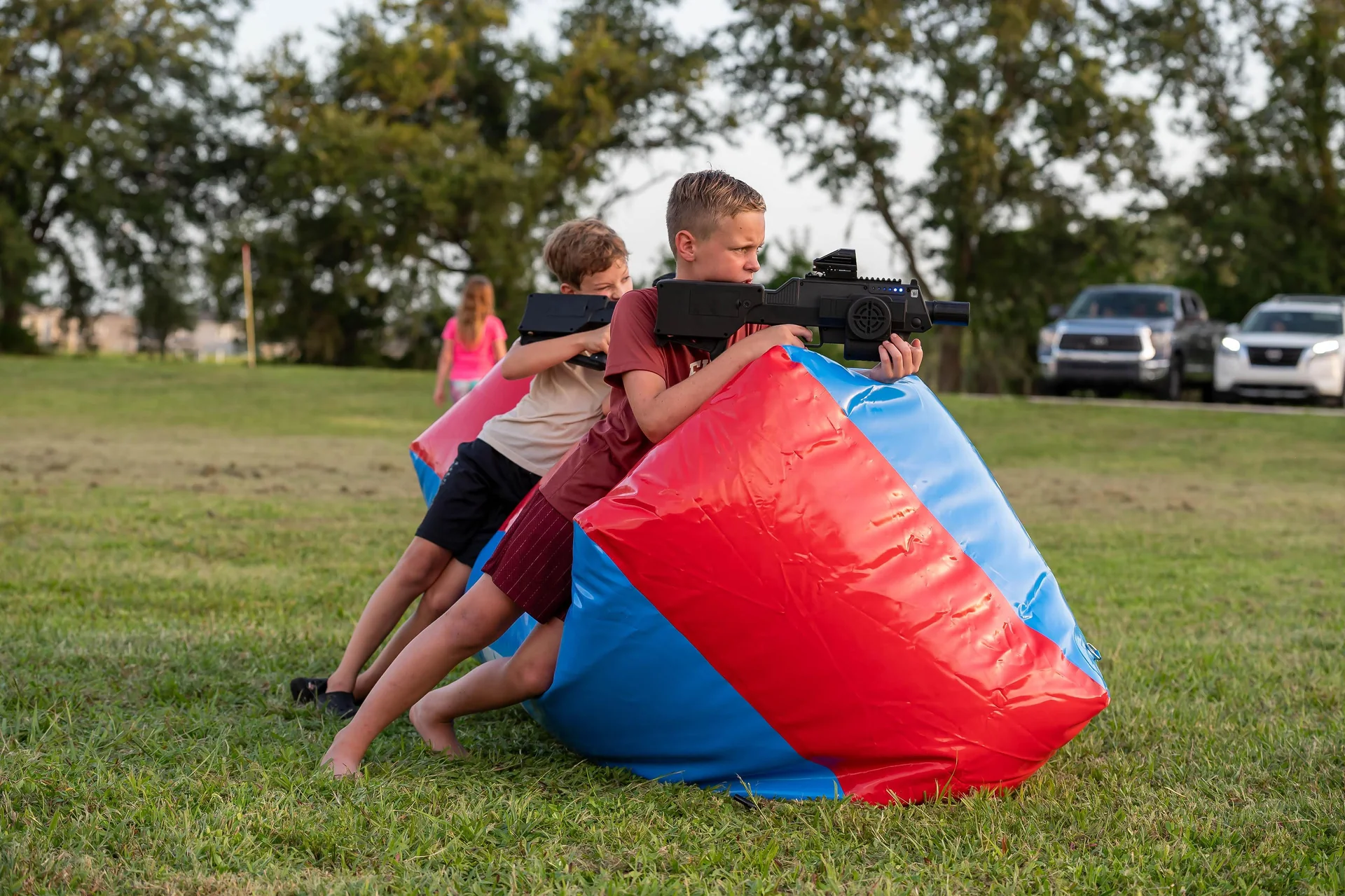 Two boys aiming Halo-inspired laser tag battle rifles from behind inflatable barricade in open field