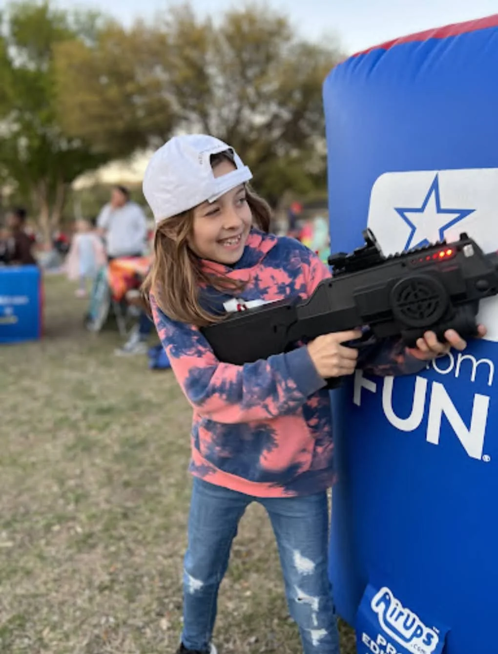 Smiling girl aiming Halo-inspired laser tag battle rifle at outdoor community event