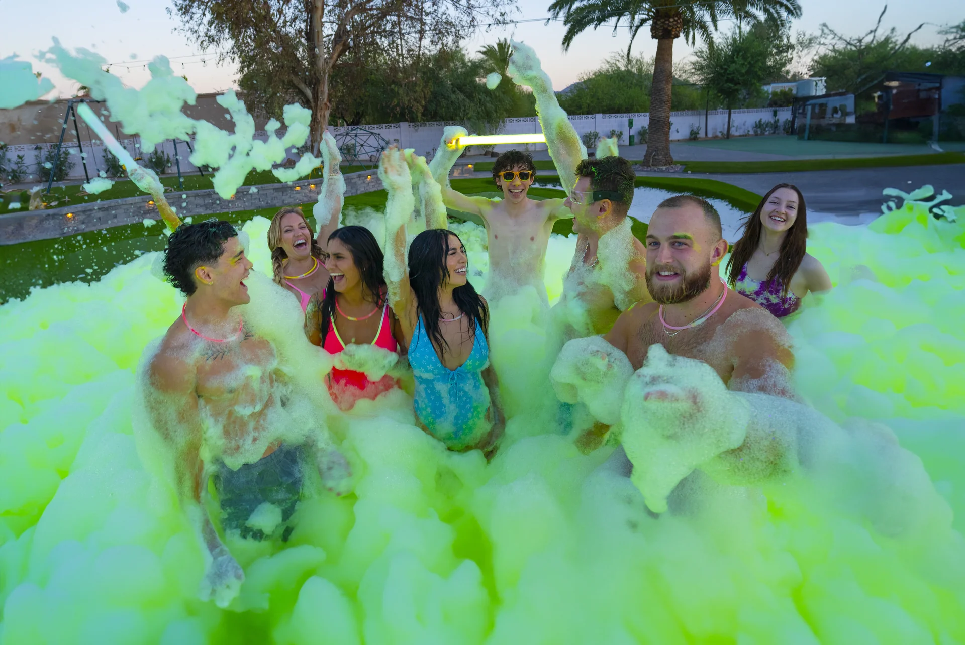 Group of friends cheering and throwing glowing green foam at a Party Rocker dusk event in Winston-Salem NC