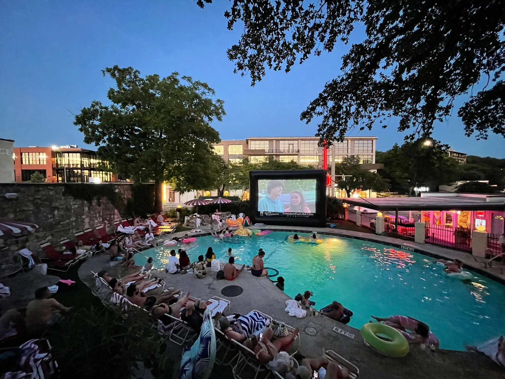 Large outdoor movie night rental at a community pool party with crowd watching a film on a giant inflatable projection screen