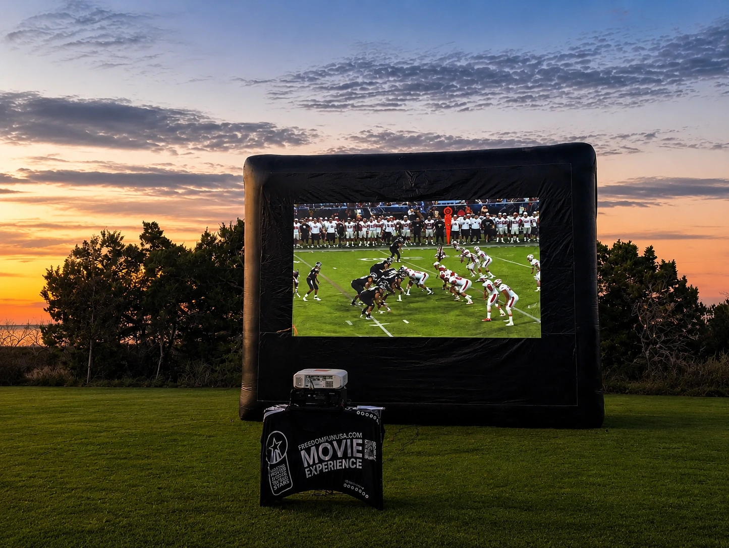 Freedom Fun USA 25ft Platinum outdoor movie screen rental Austin Texas with football game playing at sunset on green lawn with Movie Experience branded table