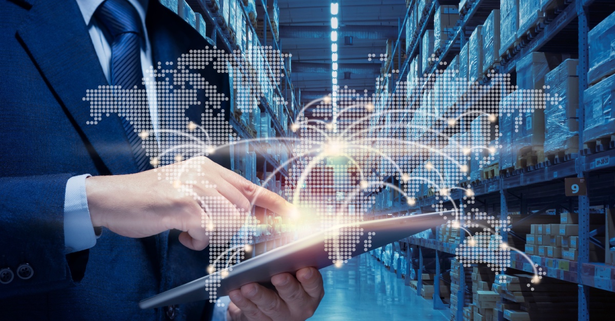 Businessman using a tablet in a warehouse aisle, with a digital world map and connection lines overlaid.