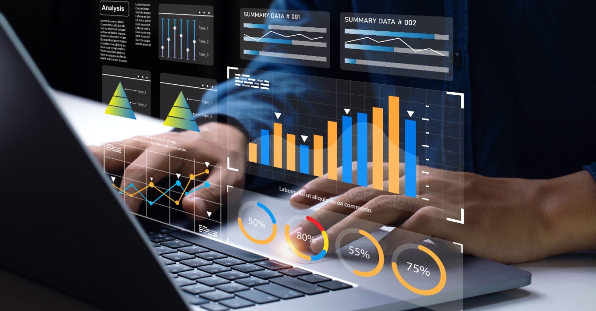 Hands typing on a laptop with holographic bar charts, line graphs and percentage gauges above the keyboard.