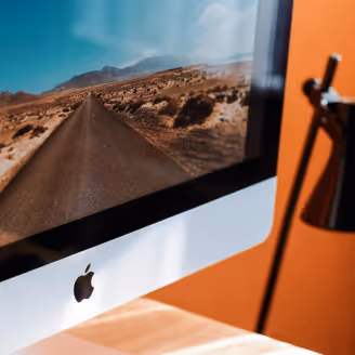 Close-up of an iMac screen displaying a desert road with mountains in the background.