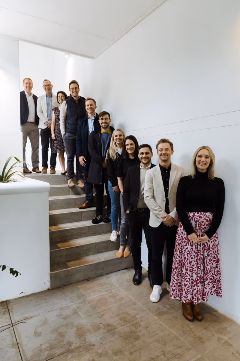 A diverse group of eleven people standing on a staircase indoors, smiling toward the camera.