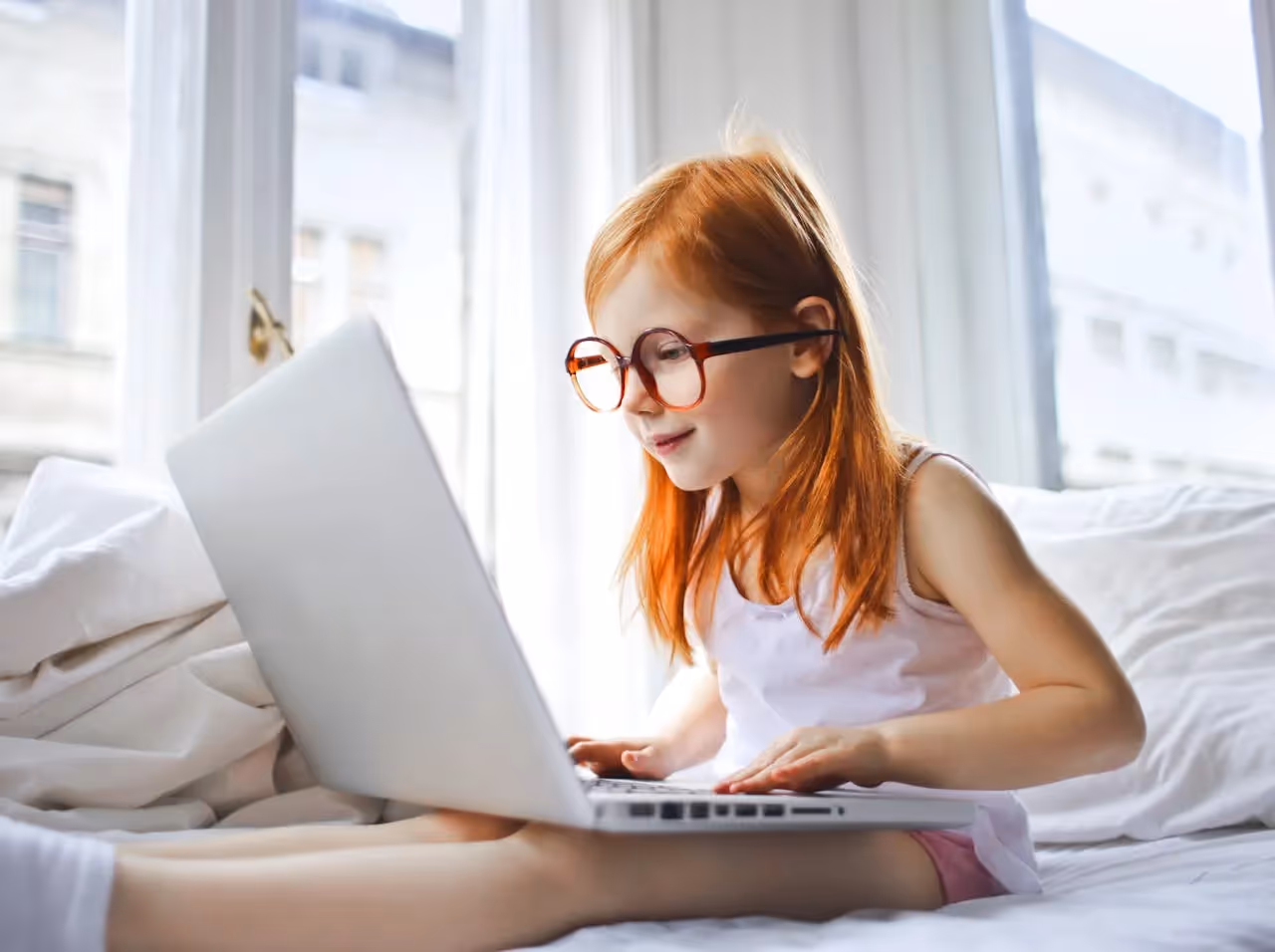 Young Girl in Glasses Sitting in Bed While Using a Laptop