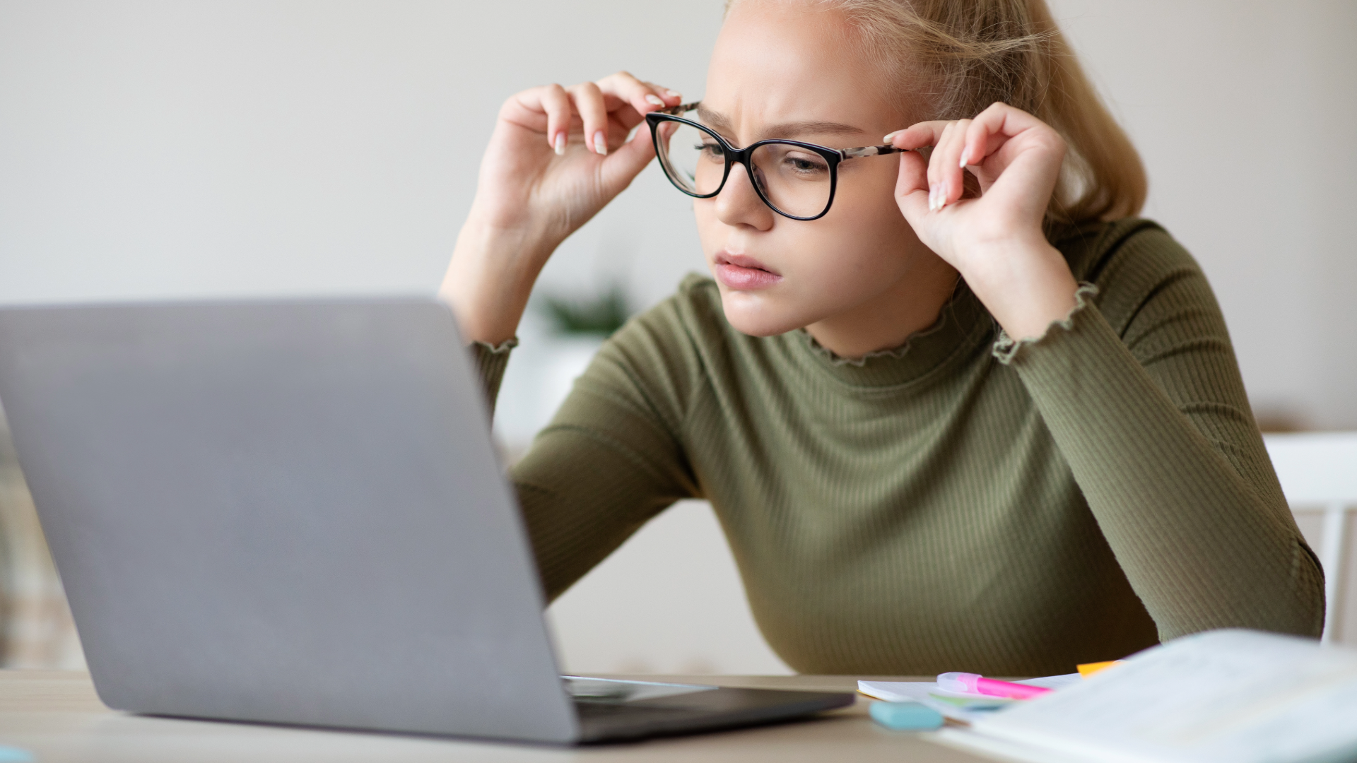 Teen girl fixing her glasses while looking at laptop screen