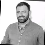 A smiling man with a beard wearing a denim shirt.
