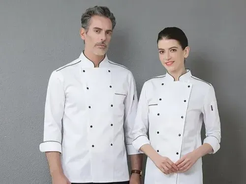 Male and female chefs wearing white double-breasted chef jackets, standing against a gray background, showcasing professional chef uniforms.