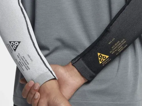 Close-up of a person's arms wearing a stylish gray shirt with contrasting black and white sleeves, featuring branded logos and text design, highlighting modern fashion details.