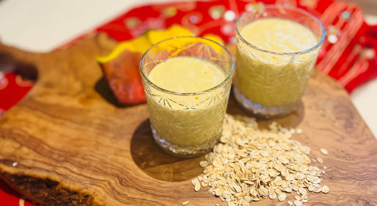 Glasses Mango lassi smoothie on a cutting board with some oats around it. 